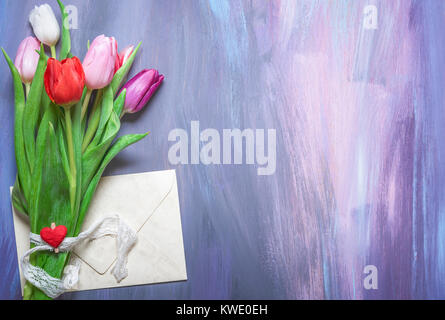 Blumenstrauß aus Tulpen mit einem spitzen Band und einem hölzernen Clip mit einem roten Herz gebunden, und einem geschlossenen Umschlag, auf lila Holz- Hintergrund. Stockfoto