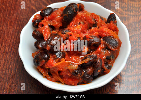 Vegetarisches Gericht der gedünstete Karotte und schwarze Bohnen mit Tomatensauce in eine weiße Keramik Schüssel auf einem Holztisch close-up. Stockfoto