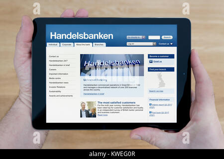 Ein Mann schaut auf die Svenska Handelsbanken Website auf seinem iPad tablet device, Schuß gegen einen hölzernen Tisch top Hintergrund (nur redaktionelle Nutzung) Stockfoto