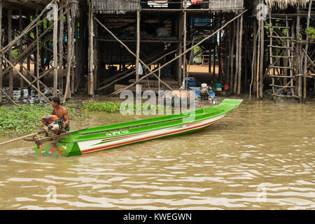 Ein muskulöser Kambodschanischen asiatischer Mann zu Fuß in den Tonle Sap See Aue braunes Wasser, neben Motor angetrieben Lange Dünne grüne Boot, Kambodscha Süd-ost Stockfoto