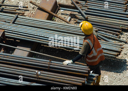 Ein Arbeiter auf einer Baustelle in der Nähe von Stange aus Stahl auf einer Baustelle gestapelt Stockfoto