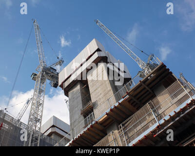 Krane arbeiten an eine große, moderne Baustelle mit konkreten Strukturen und blauer Himmel Stockfoto