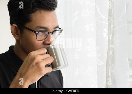 Asiatische teenage heißen Getränke während aus Fenster suchen Stockfoto
