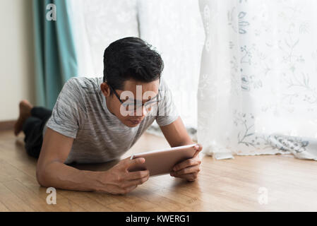 Asian teen mit digitalen tablet, während auf dem Boden in seinem Haus liegen. Freiberufler Konzept Stockfoto