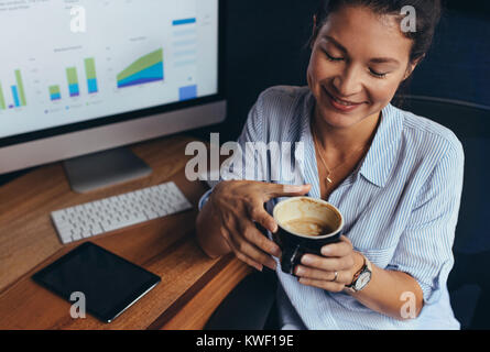 Junge geschäftsfrau an ihrem Schreibtisch und trinken Kaffee im Büro zu sitzen. Young Business Professional mit Kaffeepause. Stockfoto