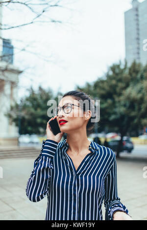 Asiatische Geschäftsfrau zu Fuß außerhalb mit Handy. Weibliche Business Professional im Freien auf city street Gespräch am Handy. Stockfoto