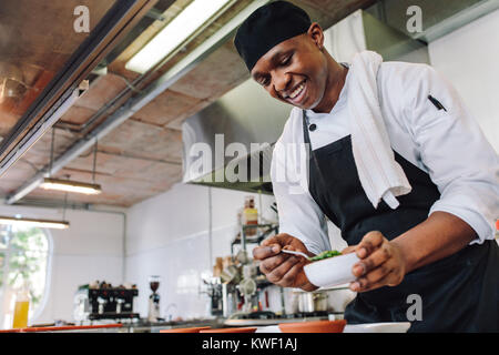 Gourmet Koch in Uniform kochen in einer gewerblichen Küche. Gerne männliche Koch Schürze tragen, steht die Arbeitsplatte in der Küche die Zubereitung von Speisen. Stockfoto