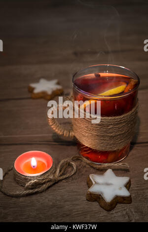 Glühwein in einem Glas Schale auf einem Holztisch mit Weihnachtsplätzchen und brennende Kerze. Stockfoto