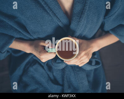 Eine junge Frau im Bademantel ist das Trinken einer Tasse Tee im Bett Stockfoto