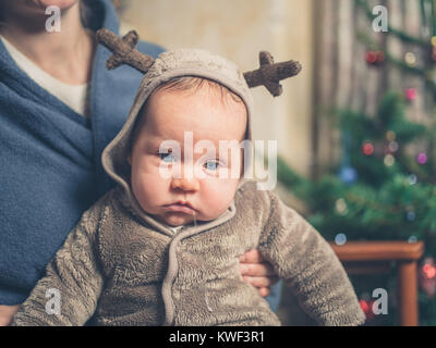 Eine traurige Baby tragen ein Rentier Outfit vor dem Weihnachtsbaum Stockfoto