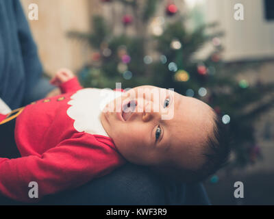 Ein glückliches Baby tragen eines santa Outfit vor dem Weihnachtsbaum Stockfoto