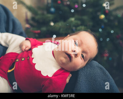 Ein Baby, das Tragen eines santa Outfit vor dem Weihnachtsbaum Stockfoto