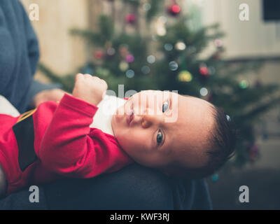 Ein Baby, das Tragen eines santa Outfit vor dem Weihnachtsbaum Stockfoto