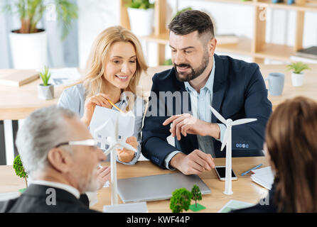 Mühle Turbinen. Clevere progressive junge Ingenieure ein schönes Modell eines Hauses am Tisch sitzen mit hübschen kleinen Miniatur Mühle Stockfoto