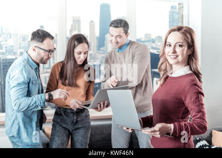 Am besten funktionieren. Sicher sehr schöne Frau, die in der Nähe von ihren Kollegen halten Sie den Laptop, und gerade auf der Suche. Stockfoto