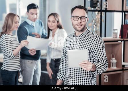 Es nehmen. Angenehme Ruhe gut aussehender Mann stand in der Nähe der Bücherschrank schauen, gerade und mit der Tablette. Stockfoto