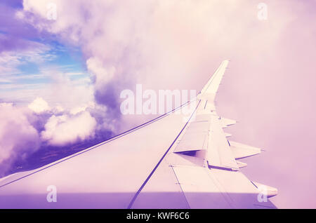 Ein Flugzeug Flügel in Wolken, die durch ein Fenster von einem Flugzeug gesehen, Farbe getonte Travel Concept Bild. Stockfoto