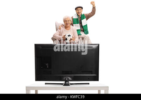 Ältere Fußballfans mit einem Fußball und einem Schal in einem Sessel sitzen und Fernsehen auf weißem Hintergrund begeistert Stockfoto