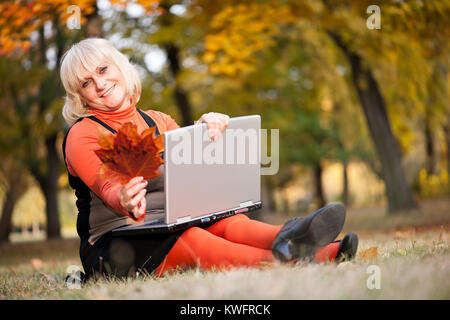 Reife Frau in einem Fall Wald mit Laptop und Blätter im Herbst in der Hand Stockfoto