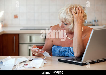 Schockiert Frau mittleren Alters in ihrer Küche am Tisch mit einem Laptop sitzen und die Kontrolle über die Preise auf die Einnahmen aus dem Supermarkt Stockfoto