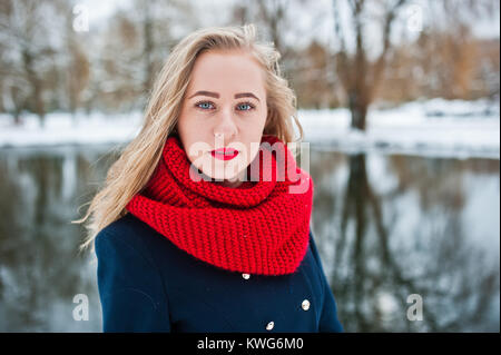 Portrai des blonden Mädchen in roten Schal und Mantel gegen zugefrorenen See im Winter Tag. Stockfoto