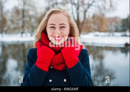 Portrai des blonden Mädchen in roten Schal und Mantel gegen zugefrorenen See im Winter Tag. Stockfoto