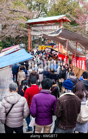 Japan, Kyoto, Yasaka Schrein. Für das neue Jahr. Verpackt Massen von Menschen zu Fuß durch eine Allee von Markt- und Imbissständen im Heiligtum Eingang zu einer massiven vermillion Torii Originalmalereien mit Laternen. Stockfoto