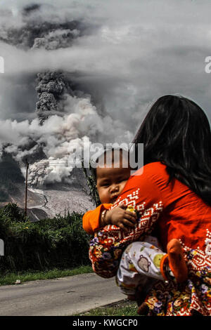 Karo, Nord Sumatra, Indonesien. 3 Jan, 2018. Indonesische Frauen mit seiner Tochter als Mount Sinabung spuckt Rauch in Karo, Nord Sumatra am 2. Januar 2018. Mount Sinabung brüllte wieder zum Leben im Jahr 2010 zum ersten Mal in 400 Jahren, nach einem bestimmten Zeitraum der Inaktivität es einmal mehr in 2013 ausbrach, und ist sehr aktiv, da geblieben. Credit: Ivan Damanik/ZUMA Draht/Alamy leben Nachrichten Stockfoto