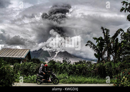 Karo, Nord Sumatra, Indonesien. 3 Jan, 2018. Indonesische Volk fahren an einer Straße als Mount Sinabung spuckt Rauch in Karo, Nord Sumatra. Mount Sinabung brüllte wieder zum Leben im Jahr 2010 zum ersten Mal in 400 Jahren, nach einem bestimmten Zeitraum der Inaktivität es einmal mehr in 2013 ausbrach, und ist sehr aktiv, da geblieben. Credit: Ivan Damanik/ZUMA Draht/Alamy leben Nachrichten Stockfoto