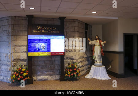 Davenport, Iowa, USA. 22. Nov 2017. Eine willkommene Board ist in der neuen Versammlung Platz im neben der Sacred Heart Cathedral in Davenport am Mittwoch, 22. November 2017 gesehen. Ein neues Kreuz auf dem Turm der Kathedrale montiert, der kurz vor dem Ende der Bauarbeiten an dem Gebäude einschließlich einer neuen Diözese an der Rückseite des Heiligen Herzens hinzugefügt. Credit: Andy Abeyta/Viererkabel - Zeiten/ZUMA Draht/Alamy leben Nachrichten Stockfoto