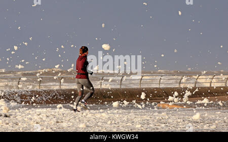 Eine Frau joggt durch Sea Foam in Blackpool als Sturm Eleanor Großbritannien mit heftigen Sturm Winde von bis zu 100 mph, verlassen Tausende von Häusern und Wohnungen, ohne Strom und schlagenden Verbindungen festgezurrt. Stockfoto