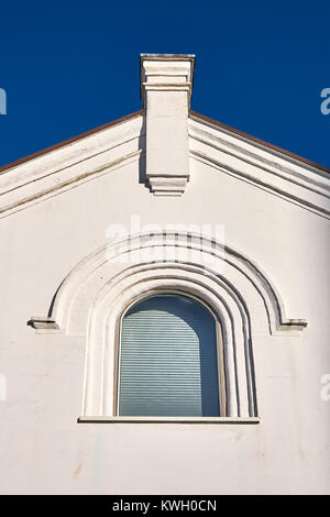 Bogenförmige Fenster in einem verputzt triangled Giebel mit einem Schornstein steigen vor blauem Himmel Stockfoto