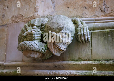 Zeitgenössische Skulptur einer Schlange mit menschlichen Händen und Schädel mit einer Goldmünze zwischen seinen Zähnen und £ Zeichen, die in der Kathedrale von Lincoln Stockfoto