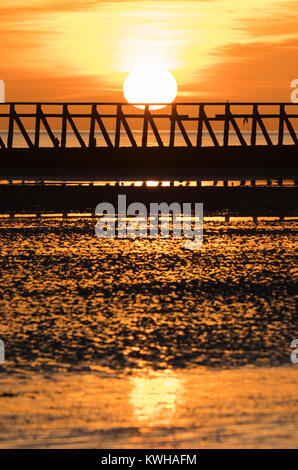 Sonnenuntergang über einem Strand mit der Ebbe im Winter, mit der Sonne im nassen Sand widerspiegelt, in Großbritannien. Stockfoto