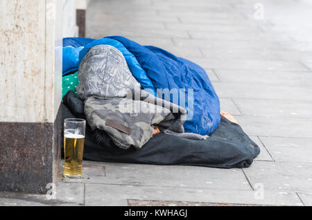 Obdachlose Person schlafen auf der Straße mit einem teilweise betrunken Tasse Bier (Alkohol) in der Nähe von Brighton, East Sussex, England, UK. Stockfoto