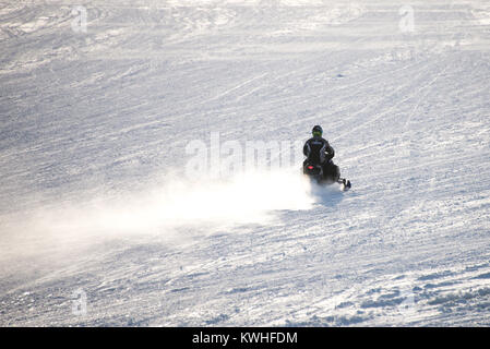 Snowmobile racing über einen schneebedeckten zugefrorenen See angenehm in den Adirondack Mountains, NY USA schüren eine Wolke von Schnee hinter ihm. Stockfoto