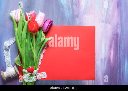 Schönen Blumenstrauß aus Tulpen mit weißen spitzen Band und einem hölzernen Clip mit einem roten Herz gebunden, auf einem leeren roten Blatt Papier gelegt. Stockfoto