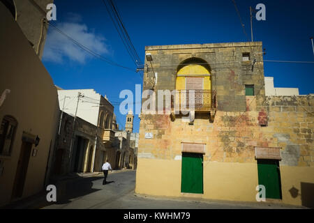 Person zu Fuß in den Straßen der Binnenschifffahrt ländliche Dorf Xewkija, Gozo, mit gewölbten St. Johannes der Täufer Kirche und traditionellen Gebäuden Stockfoto