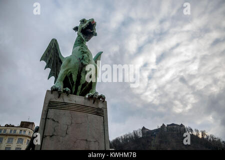 Drachen Statue auf den meisten Zmaja (Dragon Bridge) in Ljubljana, der Hauptstadt Sloweniens, mit der Burg von Ljubljana im Hintergrund. Der Drache ist EXKLU Stockfoto