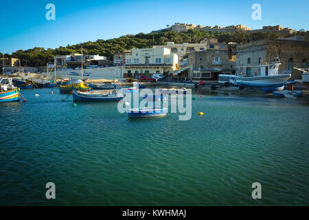 Hafen von Mgarr, Gozo im Abendlicht mit traditionellen maltesischen Fischerboote, Luzzu und Gleneagles Bar im Hintergrund Stockfoto