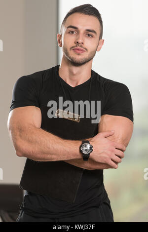 Gut aussehend Personal Trainer mit Stoppuhr In ein Fitness-Center Fitness-Studio stehen starke Stockfoto