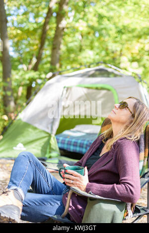 Glückliche person entspannend und unplugged mit einer Tasse Kaffee am Morgen während Herbst camping im Wald Stockfoto