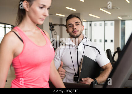 Personal Trainer zeigen junge Frau Wie zu trainieren Aerobic elliptische Walker In der Turnhalle Stockfoto