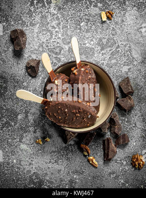Frisches Eis auf einem Stock in Schokolade mit Nüssen. Auf einem urigen Hintergrund. Stockfoto