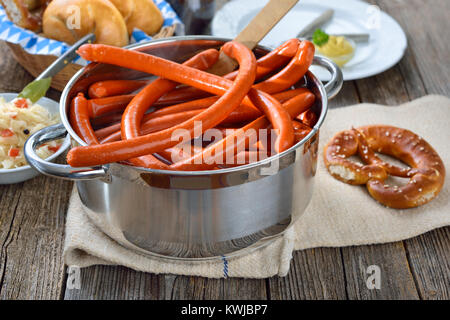 Hot Bayerische debreziner Würstchen in Edelstahl Kochtopf auf einer hölzernen Tisch mit frischen Brezeln, Brötchen serviert, würzigen Senf und Sauerkraut Stockfoto