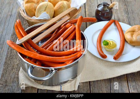 Hot debreziner Würstchen in Edelstahl Kochtopf auf einer hölzernen Tisch mit frischen Brötchen und würzigen Senf serviert. Stockfoto