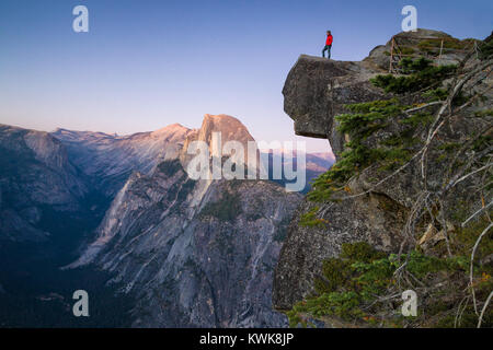 Eine furchtlose Wanderer steht auf einem überhängenden Felsen zur berühmten Half Dome am Glacier Point suchen bei Sonnenuntergang, Yosemite National Park, Kalifornien