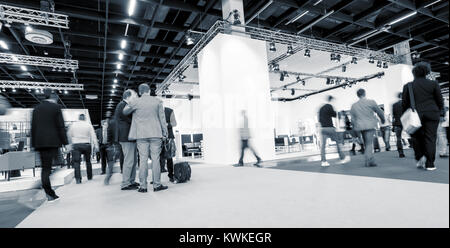 Geschäftsleute gehen an Messeständen in einer Messehalle. Stockfoto