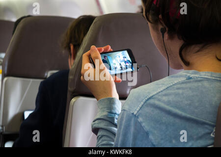 Männliche Beifahrer spielen eine Show, Film, Film oder Fernsehen auf seinem Handy - im Flugzeugmodus befindet, wird auf Maschinen des Typs Embraer air plane / Flugzeug / Flugzeug Stockfoto