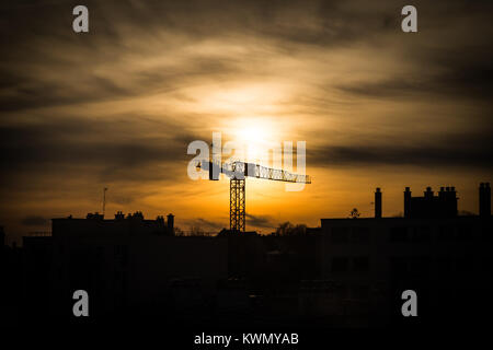 Große Industrie Kran bei Sonnenuntergang gegen eine orange Himmel über den Dächern der Stadt steigt auf die Silhouette Silhouette Stockfoto